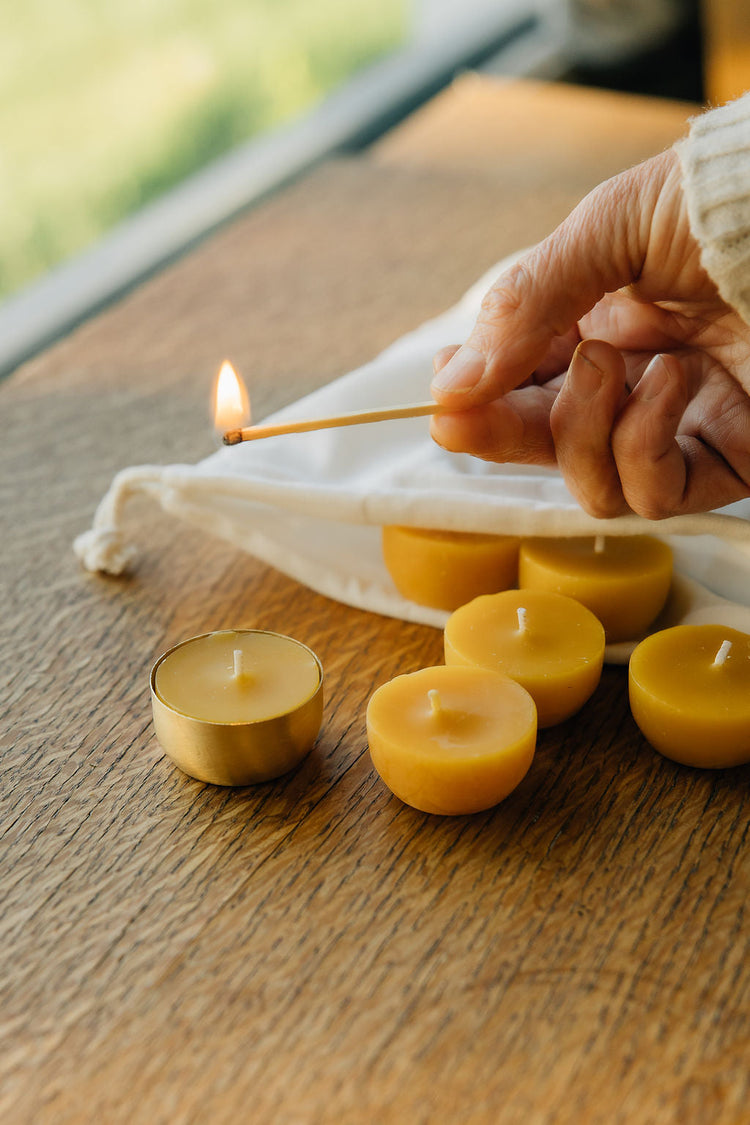 tea light candles in brass holders on a wooden table being lit with a match