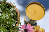 Serenibee 100% Pure Beeswax Brass Candle with flowers on a Summer garden table